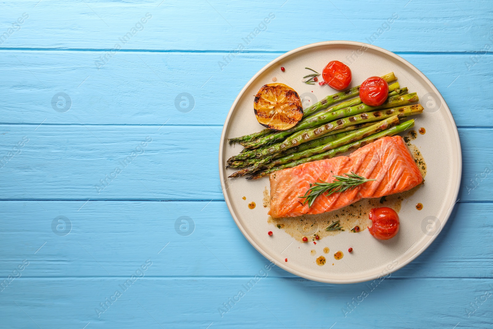 Photo of Tasty grilled salmon with tomatoes, asparagus and spices on light blue wooden table, top view. Space for text