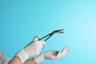 Photo of Female doctor holding bandage scissors on color background, closeup view with space for text. Medical object
