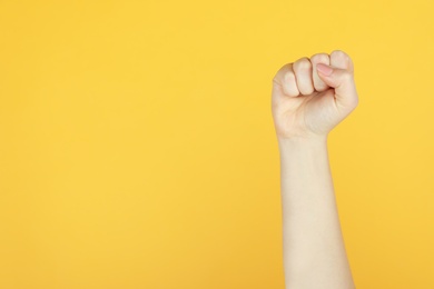 Photo of Closeup view of woman showing fist as girl power symbol on yellow background, space for text. 8 March concept