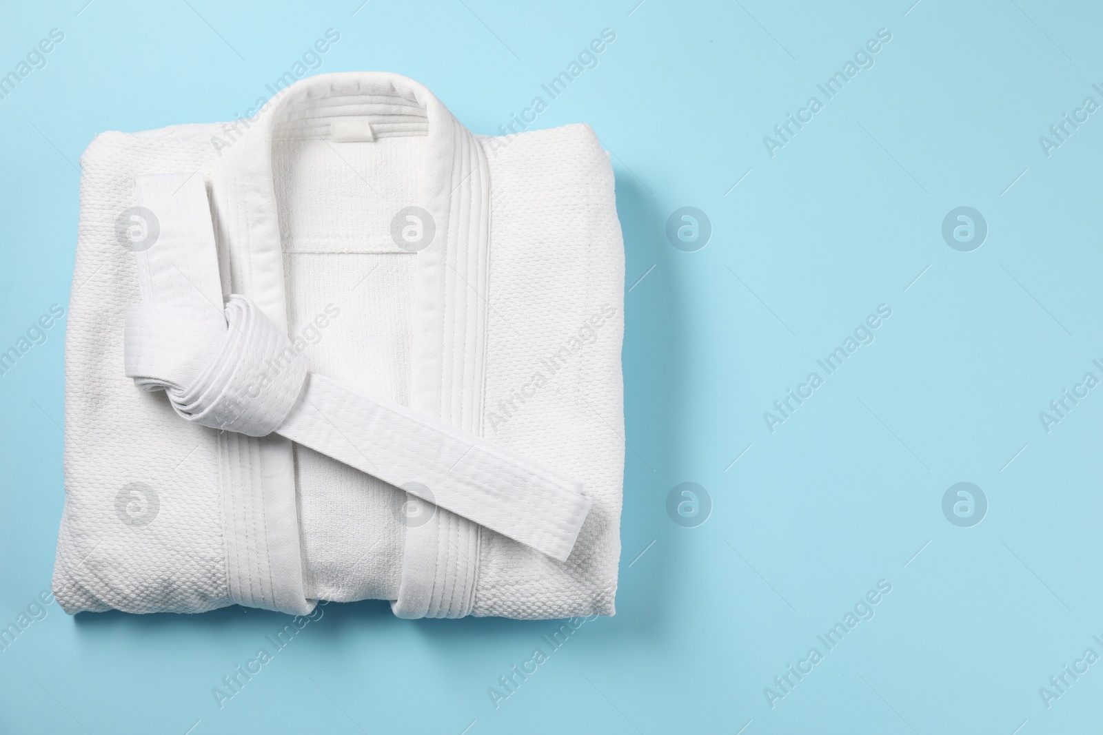 Photo of White karate belt and kimono on light blue background, top view. Space for text