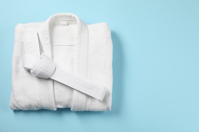 Photo of White karate belt and kimono on light blue background, top view. Space for text