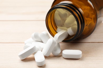 Bottle and vitamin pills on wooden table, closeup