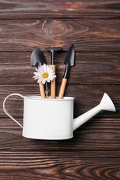 Watering can with gardening tools and flower on wooden table, top view