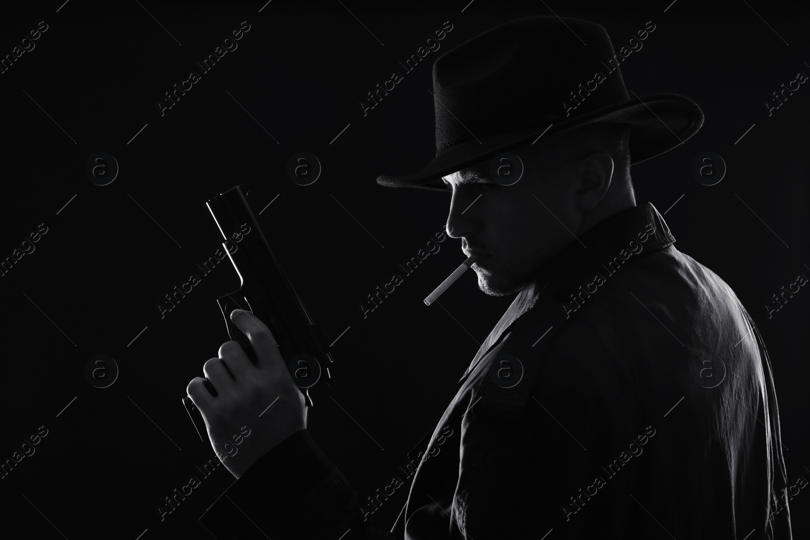 Photo of Old fashioned detective with gun smoking cigarette on dark background, black and white effect