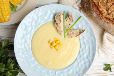 Photo of Delicious corn cream soup served on white wooden table, flat lay