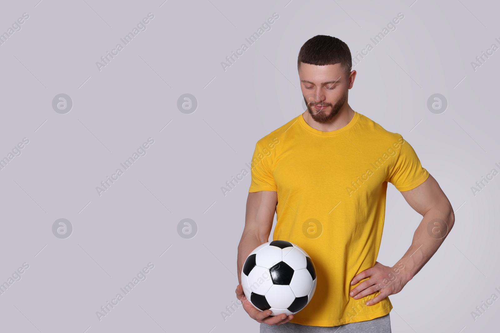 Photo of Athletic young man with soccer ball on light grey background. Space for text