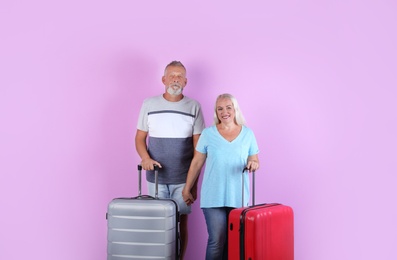 Photo of Senior couple with suitcases on color background. Vacation travel