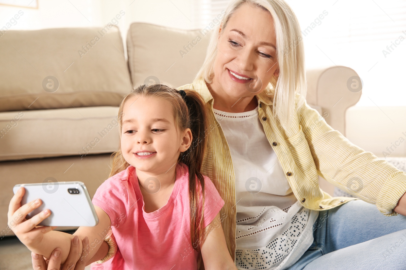 Photo of Mature woman and her little granddaughter taking selfie together at home