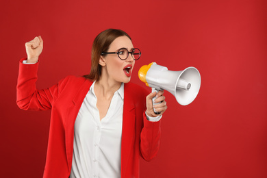 Emotional young woman with megaphone on red background