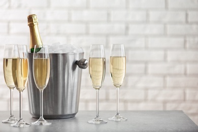 Photo of Glasses with champagne and bottle in bucket on table against brick wall