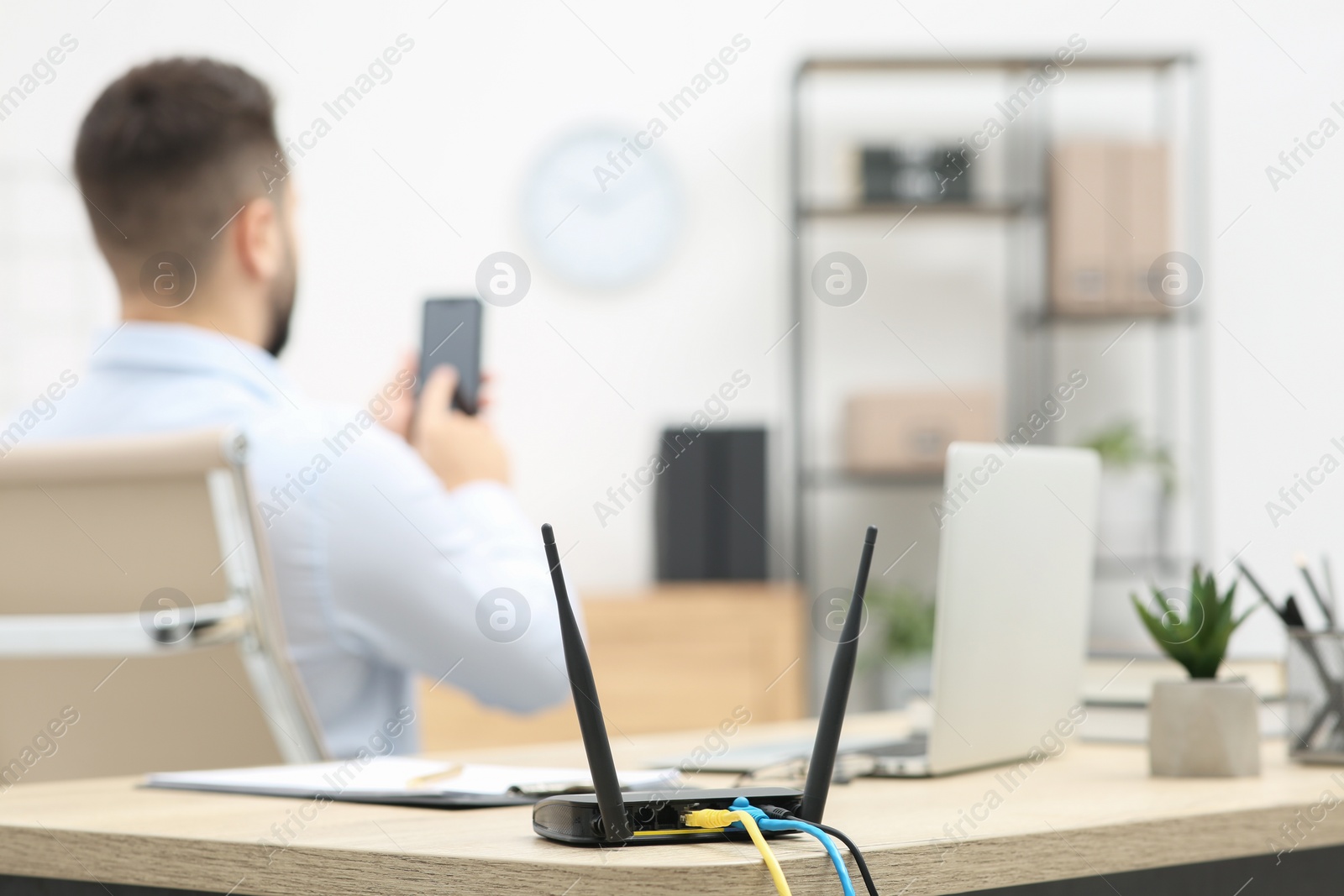 Photo of Man with smartphone working at wooden table indoors, focus on Wi-Fi router