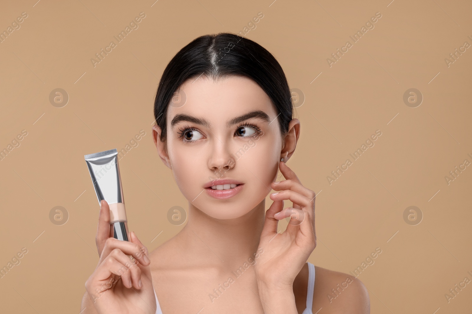 Photo of Teenage girl holding tube with foundation on beige background