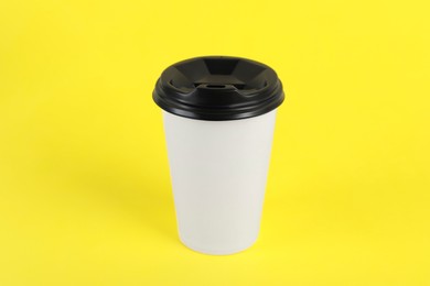 Paper cup with plastic lid on yellow background. Coffee to go