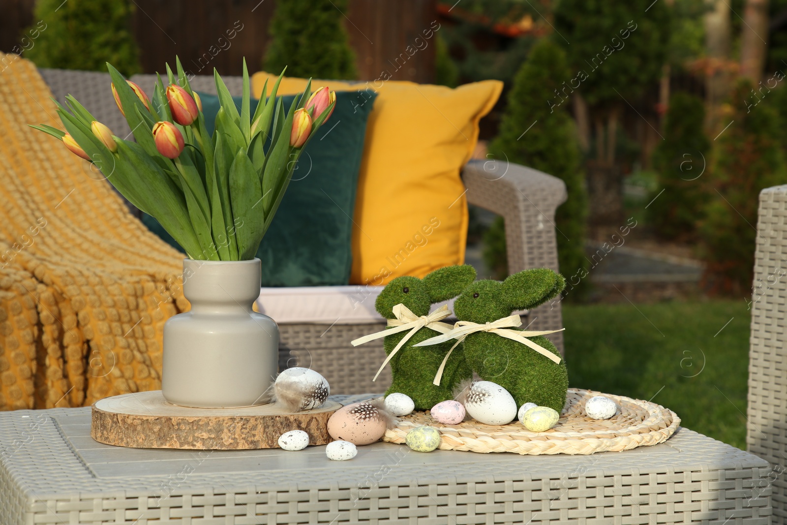 Photo of Terrace with Easter decorations. Bouquet of tulips in vase, bunny figures and decorative eggs on table outdoors