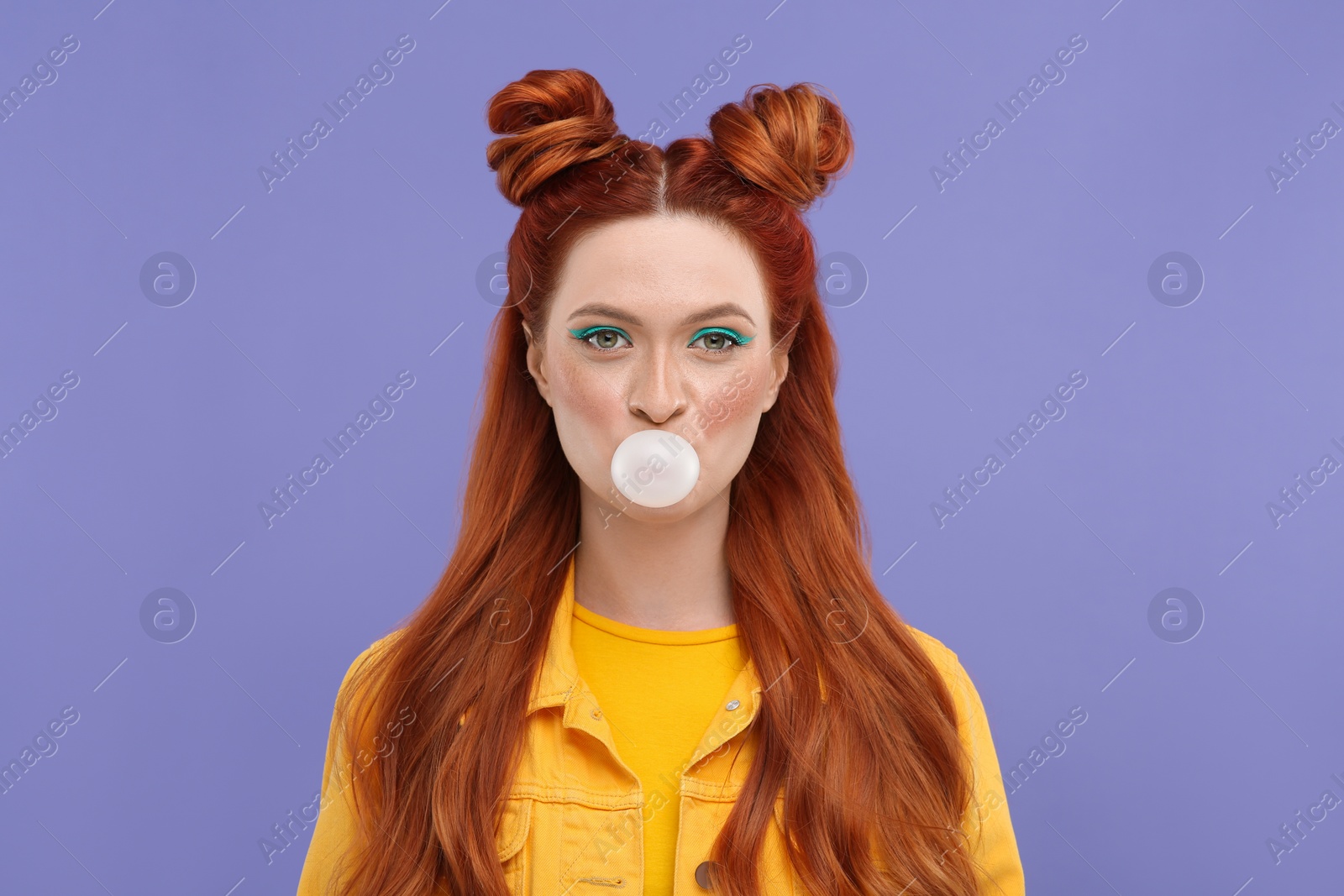 Photo of Portrait of beautiful woman with bright makeup blowing bubble gum on violet background