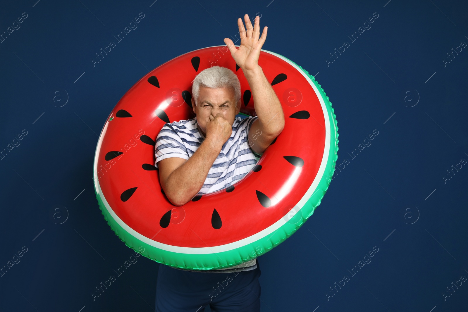 Photo of Funny mature man with bright inflatable ring on dark blue background
