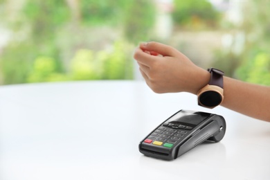 Photo of Woman using smart watch for contactless payment via terminal indoors, closeup. Space for text