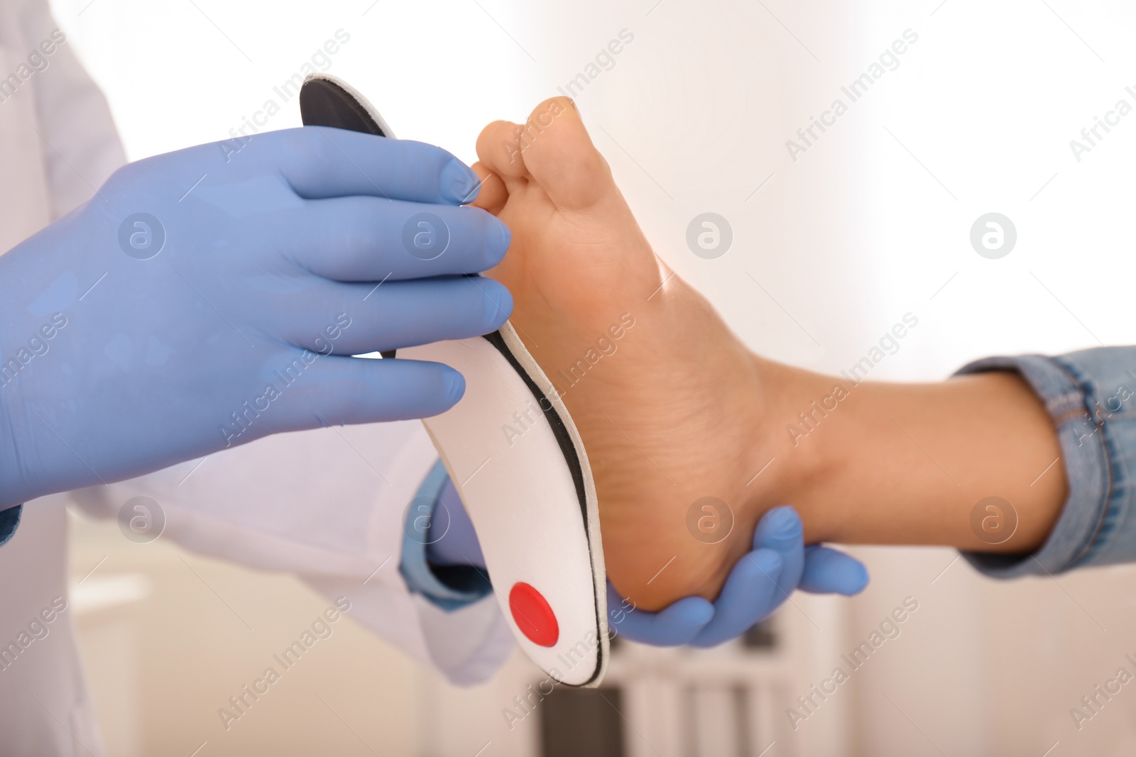 Photo of Male orthopedist fitting insole on patient's foot in clinic, closeup