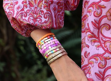 Photo of Woman wearing many stylish bracelets outdoors, closeup