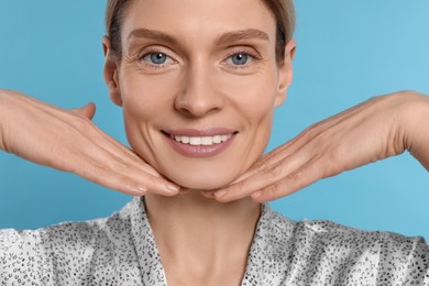 Photo of Woman massaging her face on turquoise background