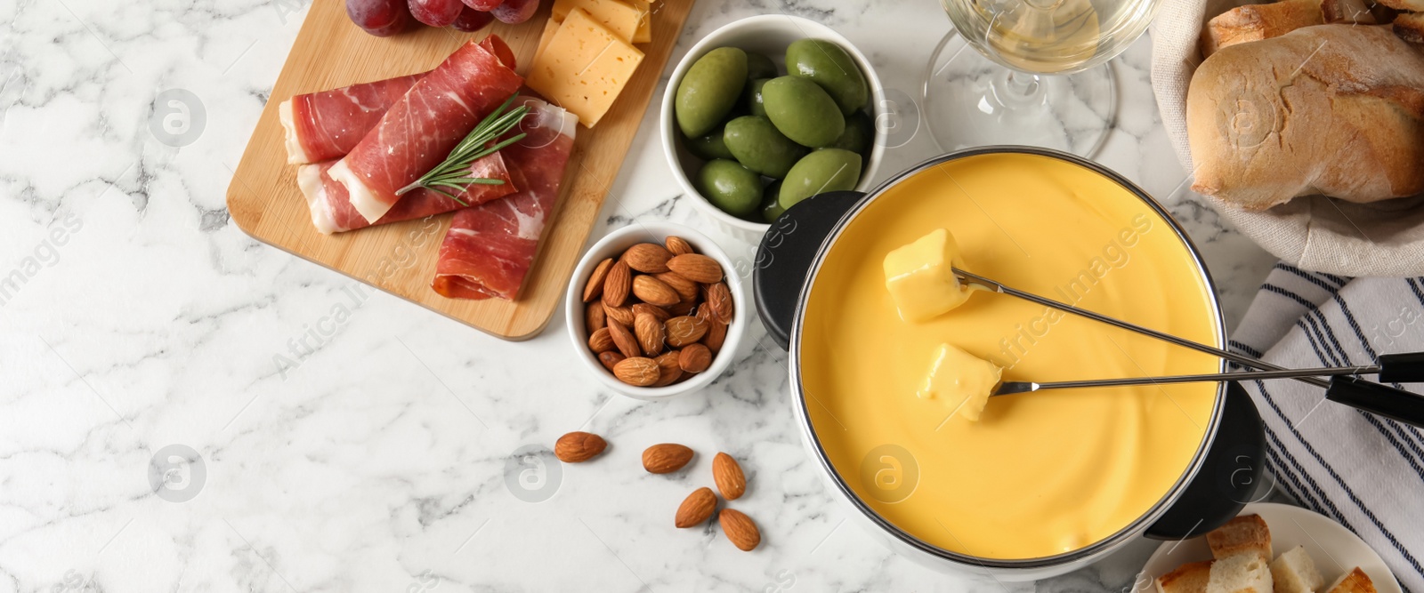 Image of Pot of tasty cheese fondue and snacks on white marble table, flat lay. Banner design