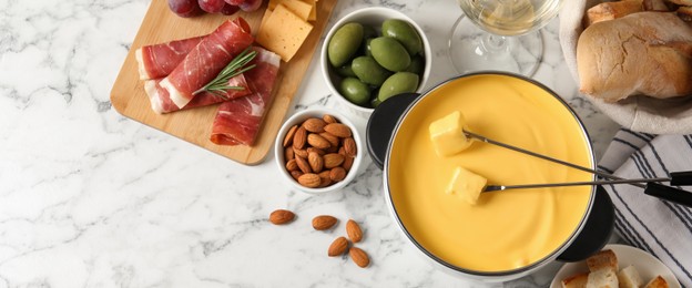 Image of Pot of tasty cheese fondue and snacks on white marble table, flat lay. Banner design