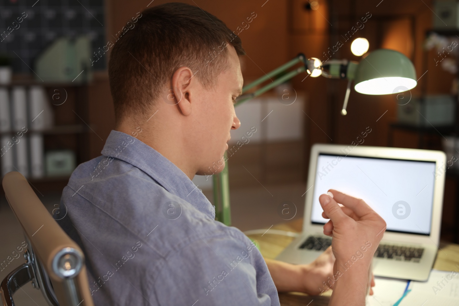 Photo of Overworked man with headache trying to take  pill in office