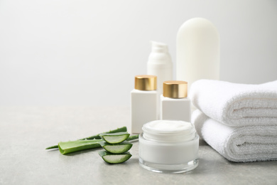 Different cosmetic products, towels and aloe on grey table