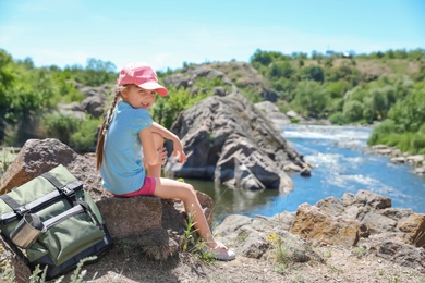 Photo of Little girl on rock near river. Summer camp