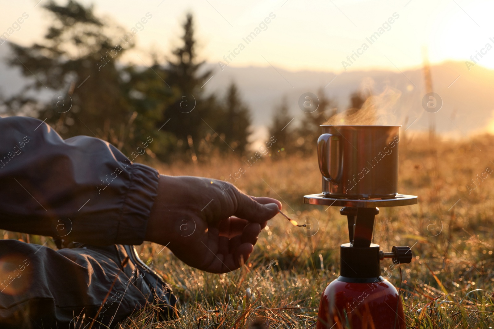 Photo of Man making hot drink with portable gas burner in mountain camping, closeup
