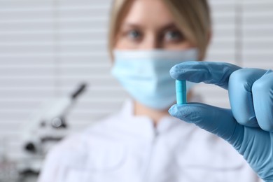 Photo of Doctor holding pill on light background, selective focus. Space for text