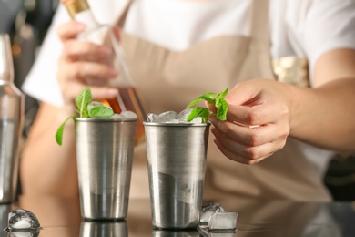 Photo of Bartender preparing delicious mint julep cocktail at table
