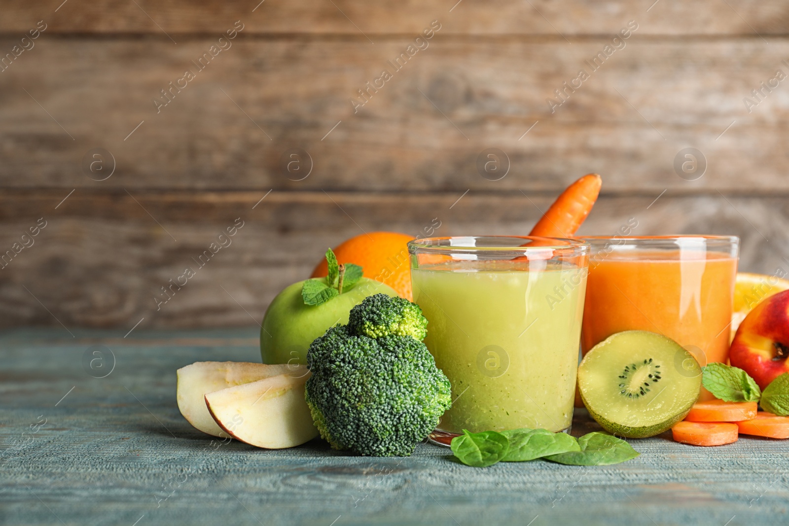 Photo of Glasses of delicious juices and fresh ingredients on blue wooden table. Space for text