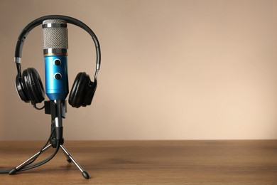 Photo of Microphone and modern headphones on wooden table against beige background, space for text