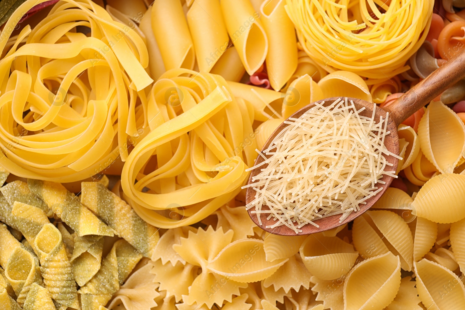 Photo of Wooden spoon and different types of pasta as background, top view