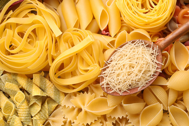 Wooden spoon and different types of pasta as background, top view