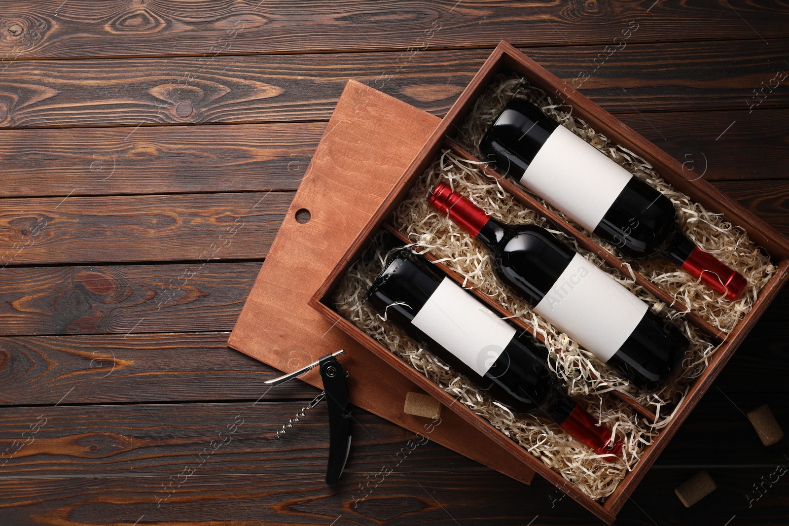 Photo of Box with wine bottles, corkscrew and corks on wooden table, flat lay. Space for text