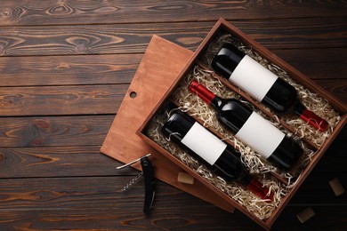 Box with wine bottles, corkscrew and corks on wooden table, flat lay. Space for text