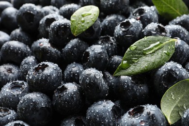 Photo of Wet fresh blueberries with green leaves as background, closeup