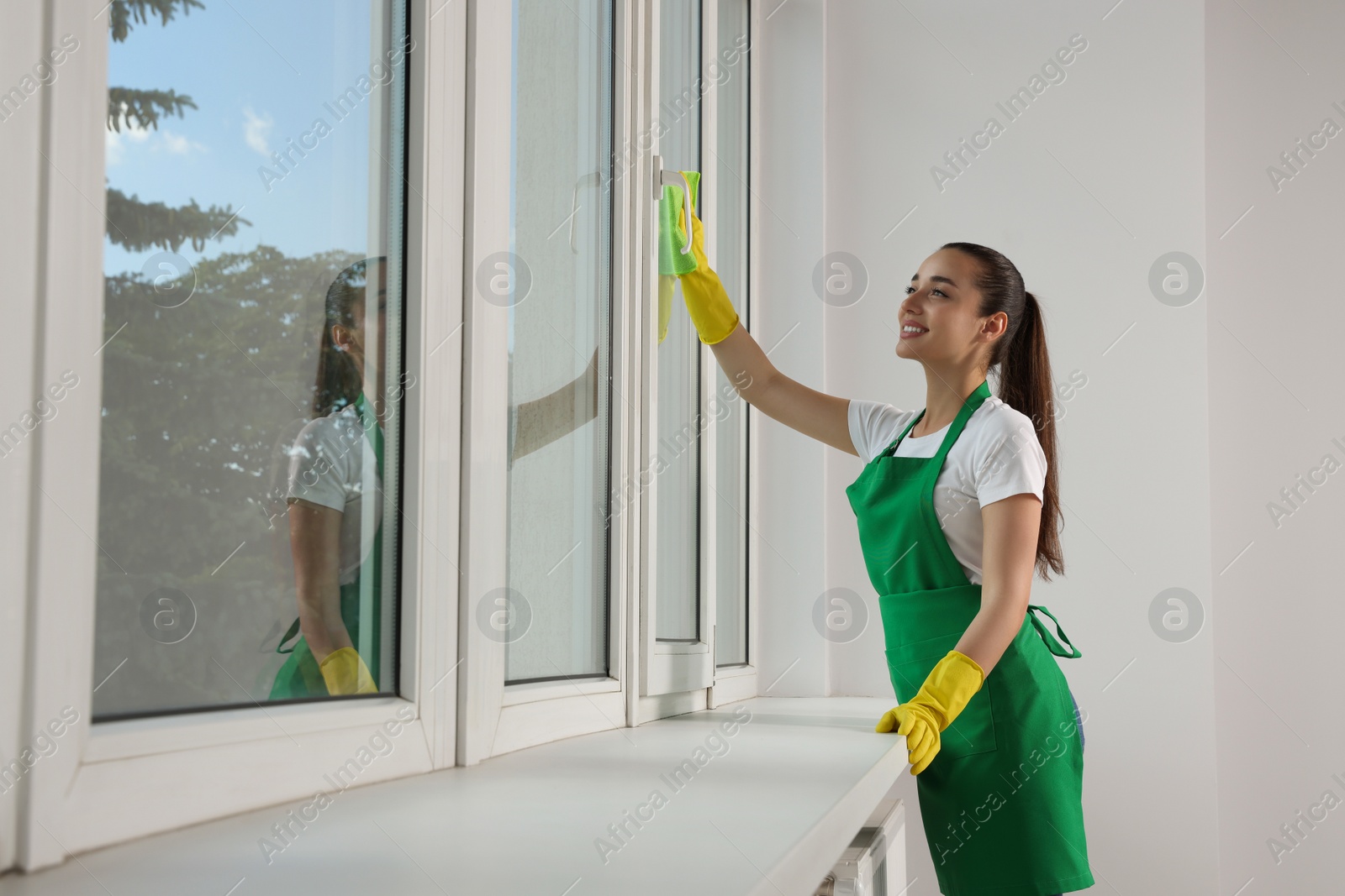 Photo of Happy young woman cleaning window glass with rag indoors