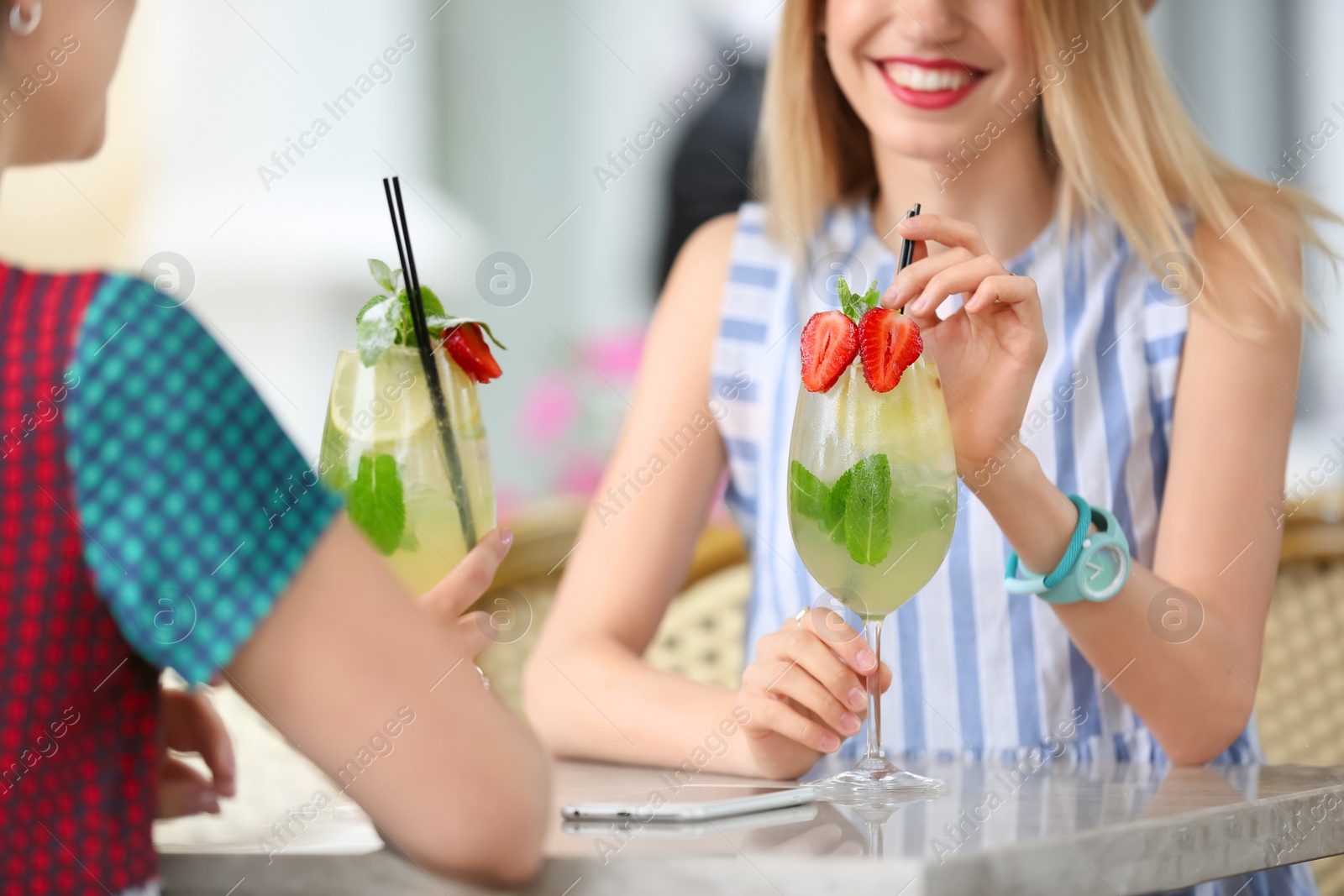 Photo of Young women with glasses of tasty lemonade in open-air cafe