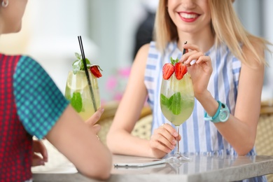 Young women with glasses of tasty lemonade in open-air cafe