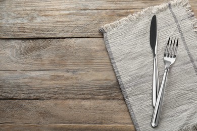 Photo of Fork, knife and napkin on wooden table, top view with space for text. Stylish shiny cutlery set