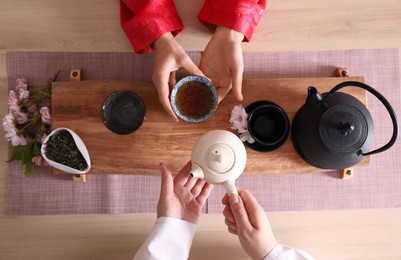 Master and guest tea during traditional ceremony at wooden table, top view