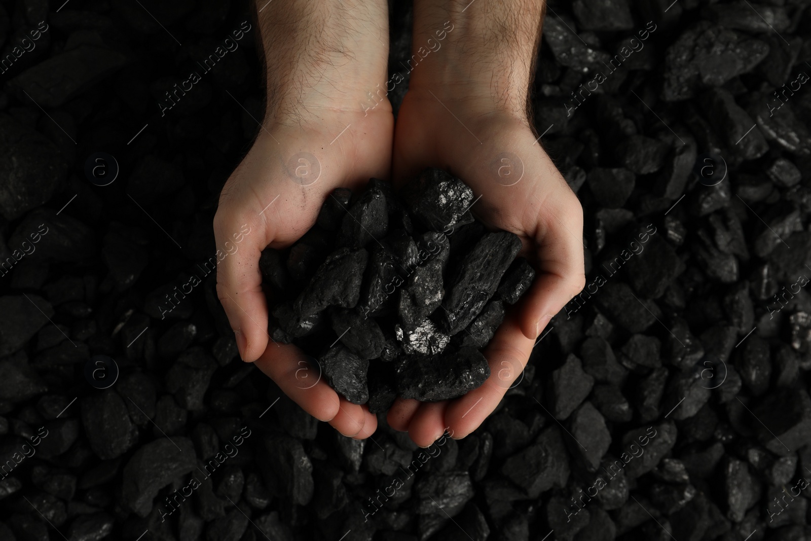 Photo of Man holding coal in hands over pile, top view