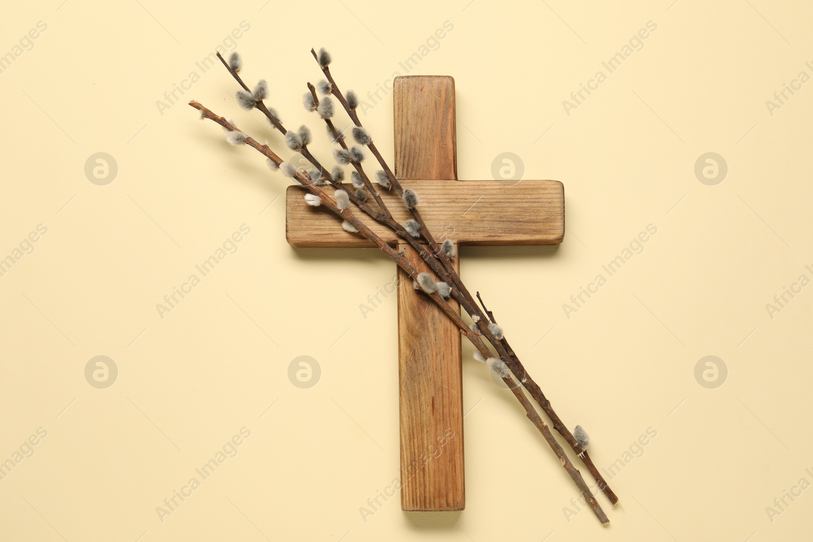 Photo of Wooden cross and willow branches on beige background, top view. Easter attributes