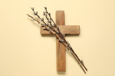 Wooden cross and willow branches on beige background, top view. Easter attributes