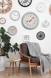Photo of Comfortable furniture, beautiful houseplant and collection of different clocks on white wall in room