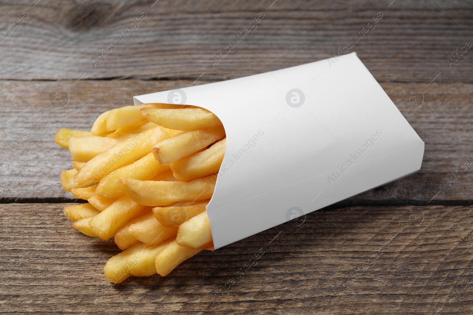 Photo of Delicious french fries in paper box on wooden table, closeup