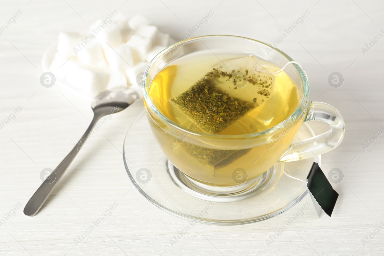 Photo of Tea bag in cup of hot water on white wooden table